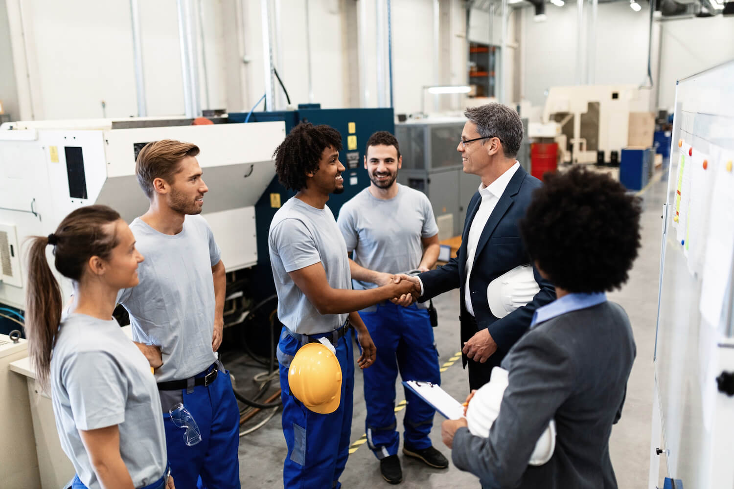 Happy corporate manager shaking hands with a worker while visiting a factory
