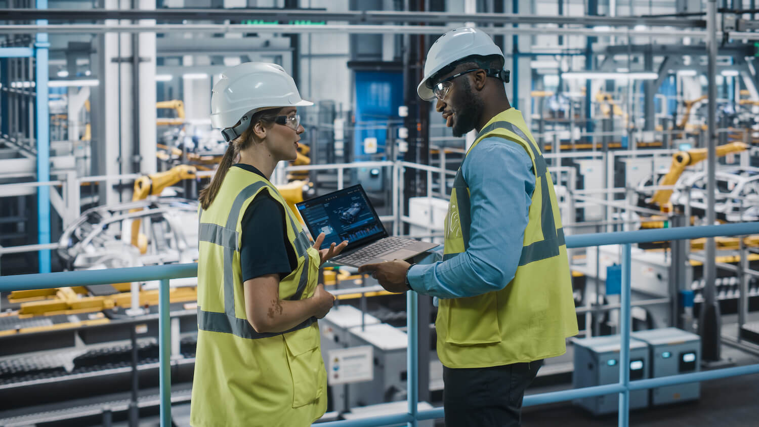 Male Specialist and Female Car Factory Engineer in High Visibility Vests Using Laptop Computer